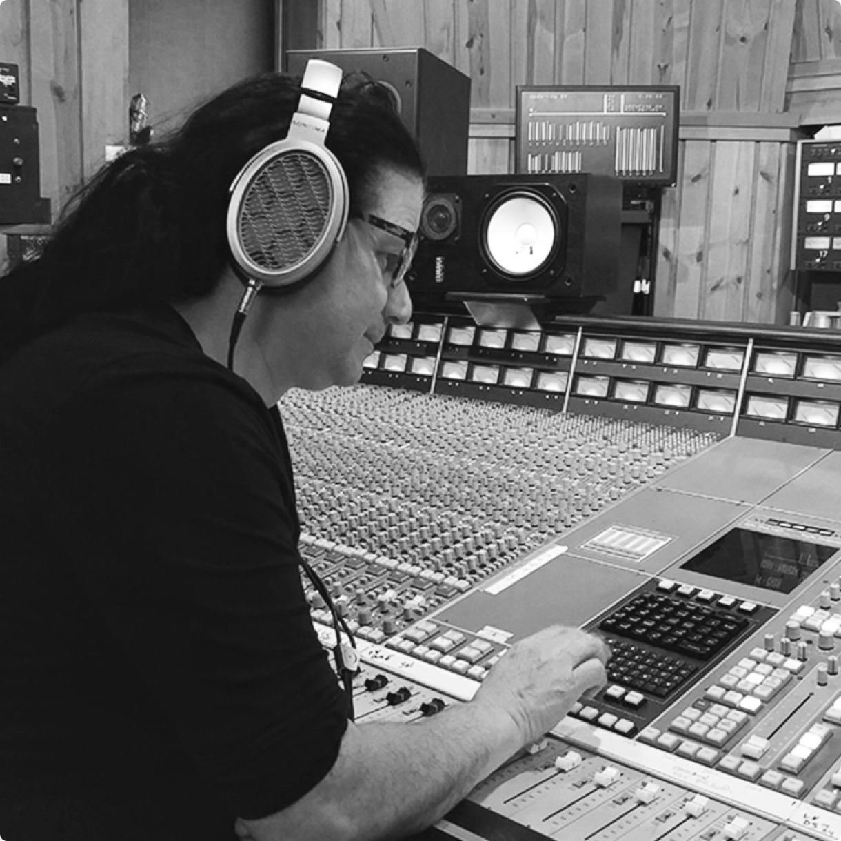 A middle-aged man smiling whilst listening to music through the Sonoma Headphones at his professional mixing desk